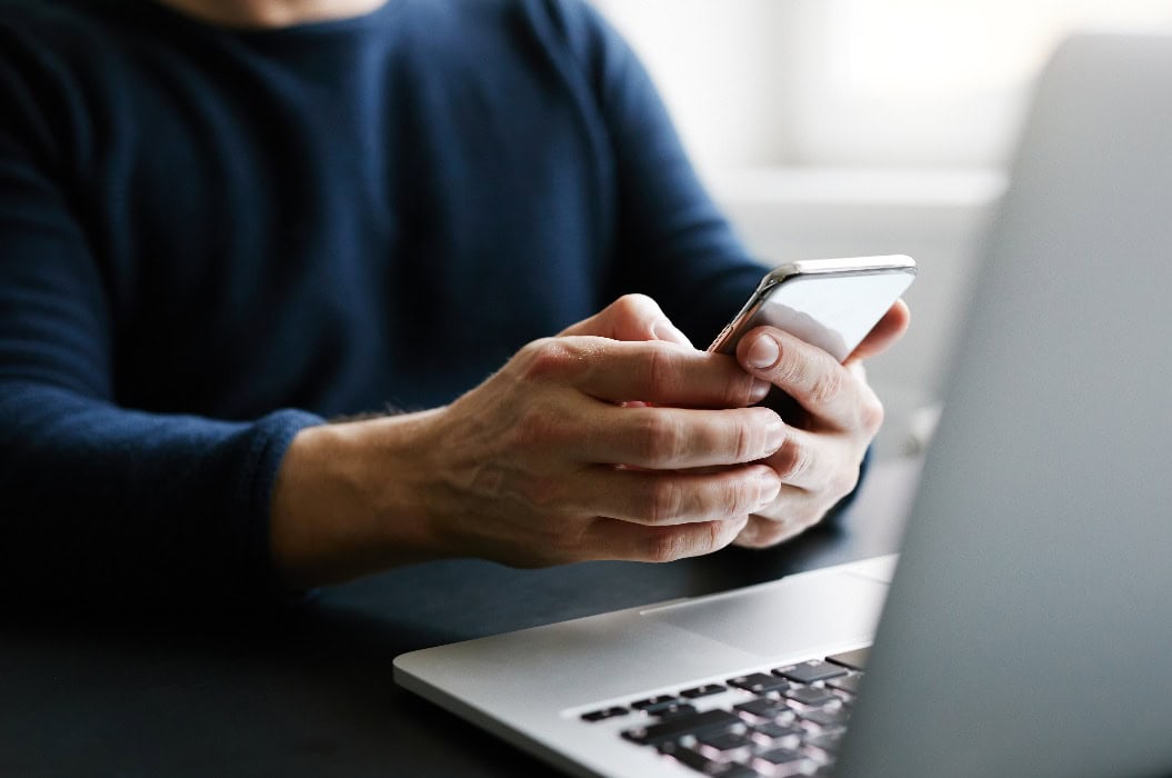 Mann mit Mobiltelefon und Laptop im Büro